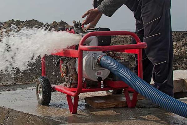 Bombas de Agua de Superficie Hombre arrancando una motobomba de agua a gasolina que suelta agua